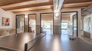 Un grand espace intérieur doté d’une table de ping-pong, de murs en pierre et offrant une vue sur un patio extérieur.