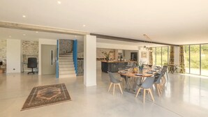 Une cuisine moderne et spacieuse avec un îlot central, un coin repas doté d’une longue table et de chaises, et un escalier agrémenté de touches de bleu.