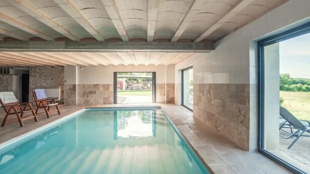 Une piscine avec un mur en pierre et une vue sur l’extérieur.