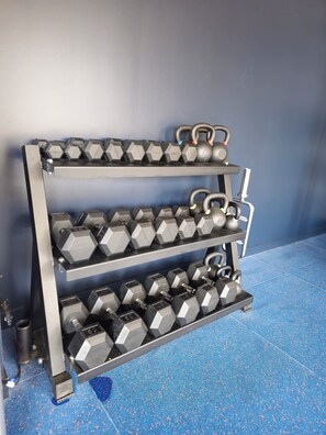 Estante de metal con mancuernas hexagonales y kettlebells frente a una pared azul.