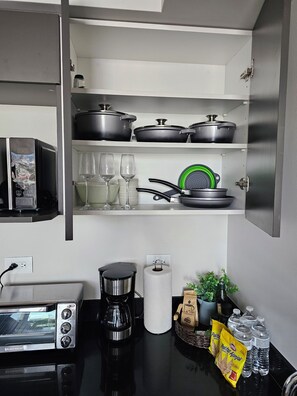 Una cocina con tostadora, cafetera y ollas sobre estantes.