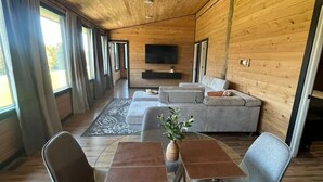 A modern interior with a wooden ceiling, a sofa set, a TV, and a dining area with chairs and a table. - Meadow Ridge Apartment — Minutes to Salmon River (Altmar)