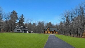 A two-story log cabin with a large porch and a separate garage, surrounded by a well-maintained lawn and trees. - Meadow Ridge Apartment — Minutes to Salmon River (Altmar)