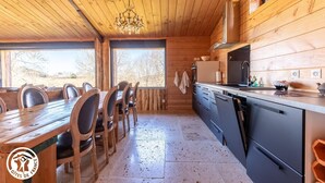 L’intérieur d’une cabane en bois comprend une table à manger, des chaises, une cuisine équipée d’appareils modernes et de grandes fenêtres.