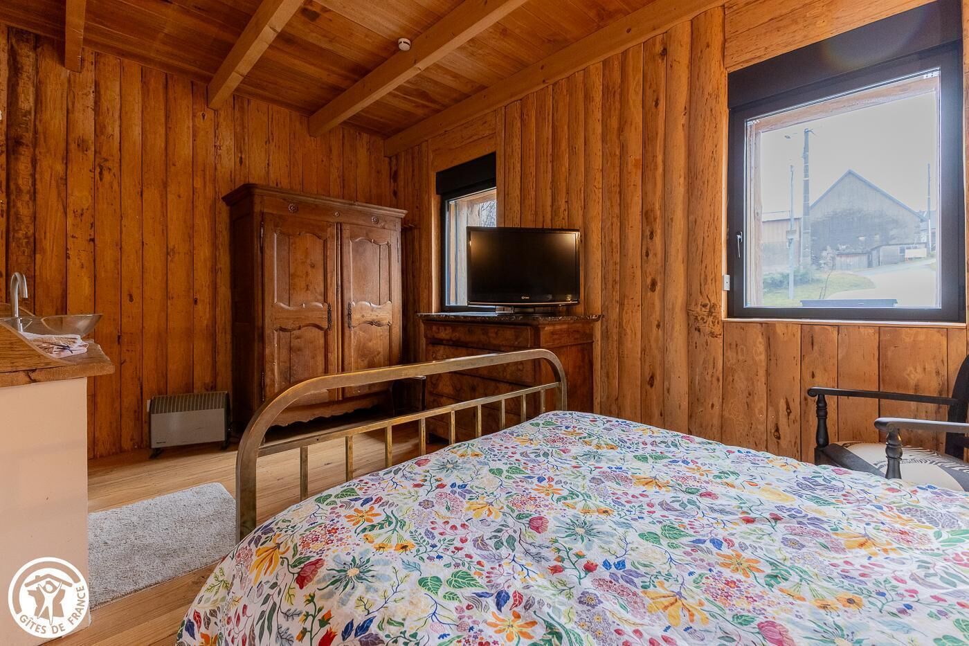 Een houten kamer met een bed, een televisie en een raam met uitzicht op een gebouw.