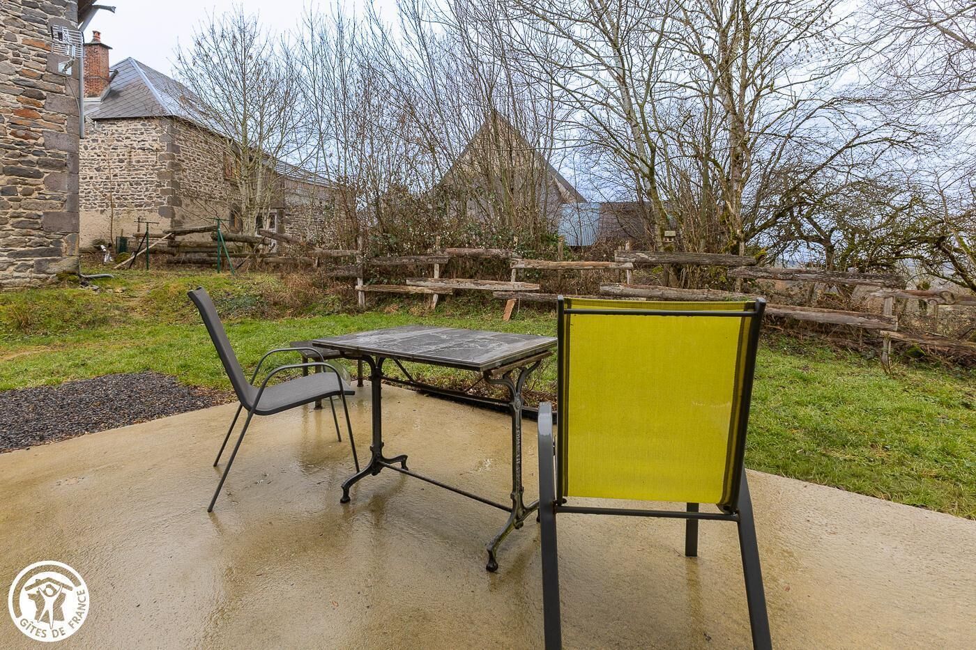 Eine Terrasse mit Tisch und Stühlen, ein gelber Stuhl und ein Steinhaus im Hintergrund.