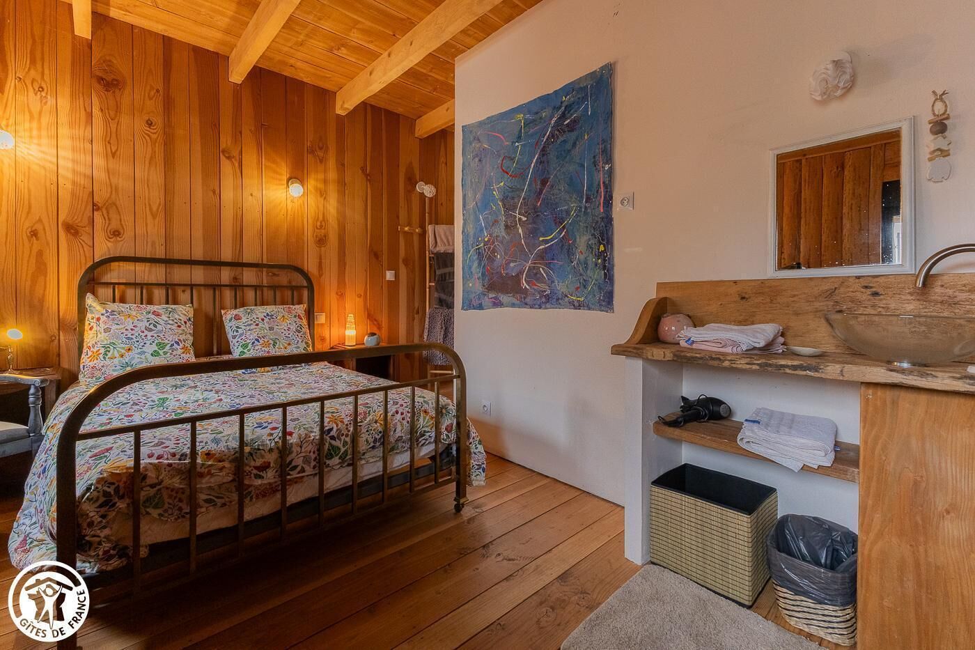 Een houten slaapkamer met een bed, een houten dressoir met een wastafel en een schilderij aan de muur.