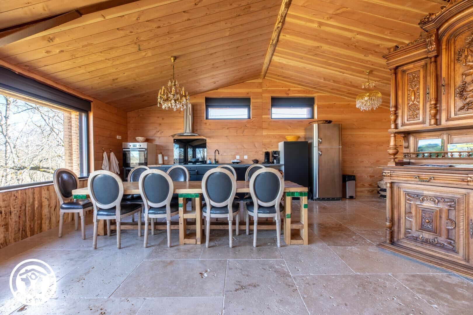 A wooden cabin interior with a dining area, kitchen, and a decorative cabinet.