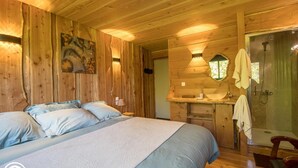 Une chambre à coucher dans une cabane en bois, comprenant un lit, une table de chevet, un miroir et une salle de bain avec un lavabo et une douche.