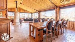 Un coin repas rustique, avec une grande table et des chaises en bois, une cheminée et une vue sur l’extérieur.
