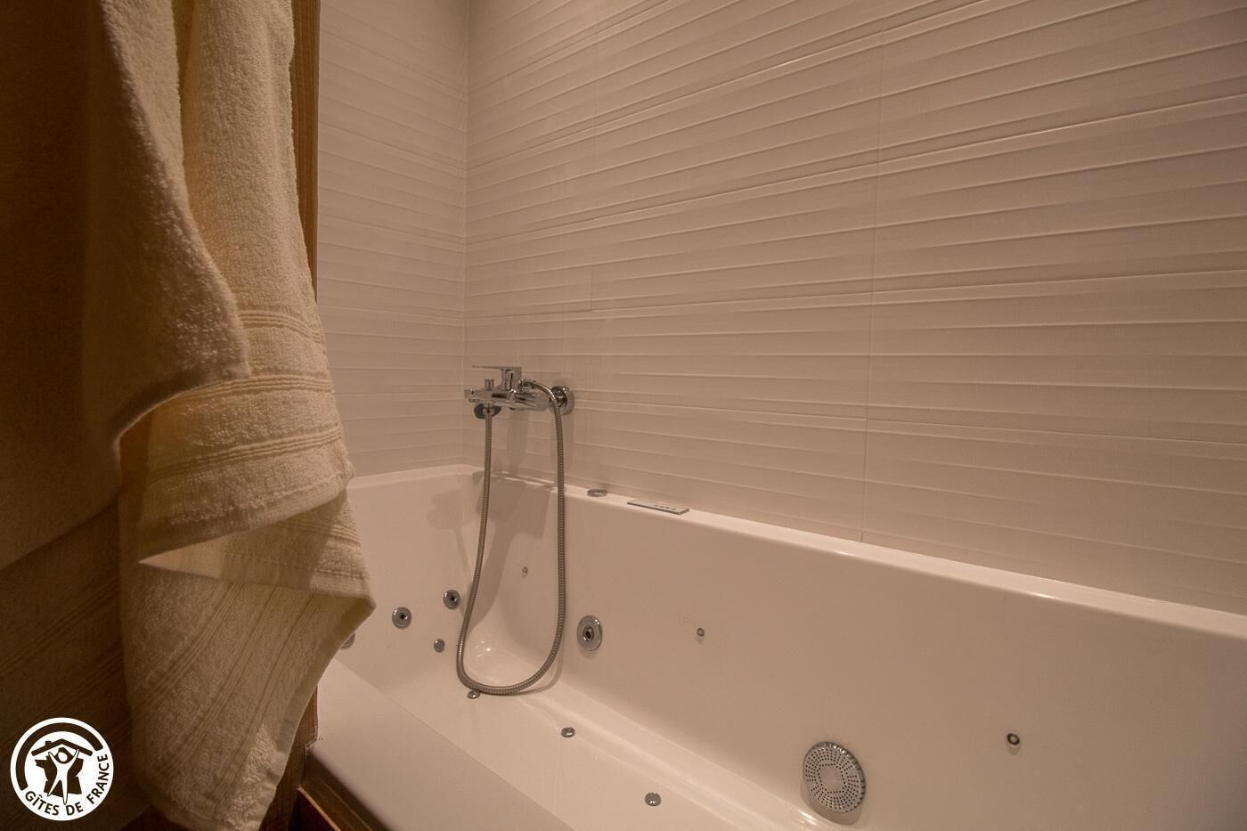 A bathroom with a bathtub, a shower head, and a towel hanging on the wall.