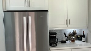 A kitchen with white cabinets, a stainless steel refrigerator, a coffee maker, and a wine bottle. - Florida Condo for Monthly rental Gated Golf Community available MarchApril 2026. (Fort Myers)