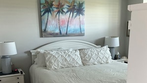 A bedroom with a bed, nightstands, a ceiling fan, a painting of palm trees, and a white dresser. - Florida Condo for Monthly rental Gated Golf Community available MarchApril 2026. (Fort Myers)