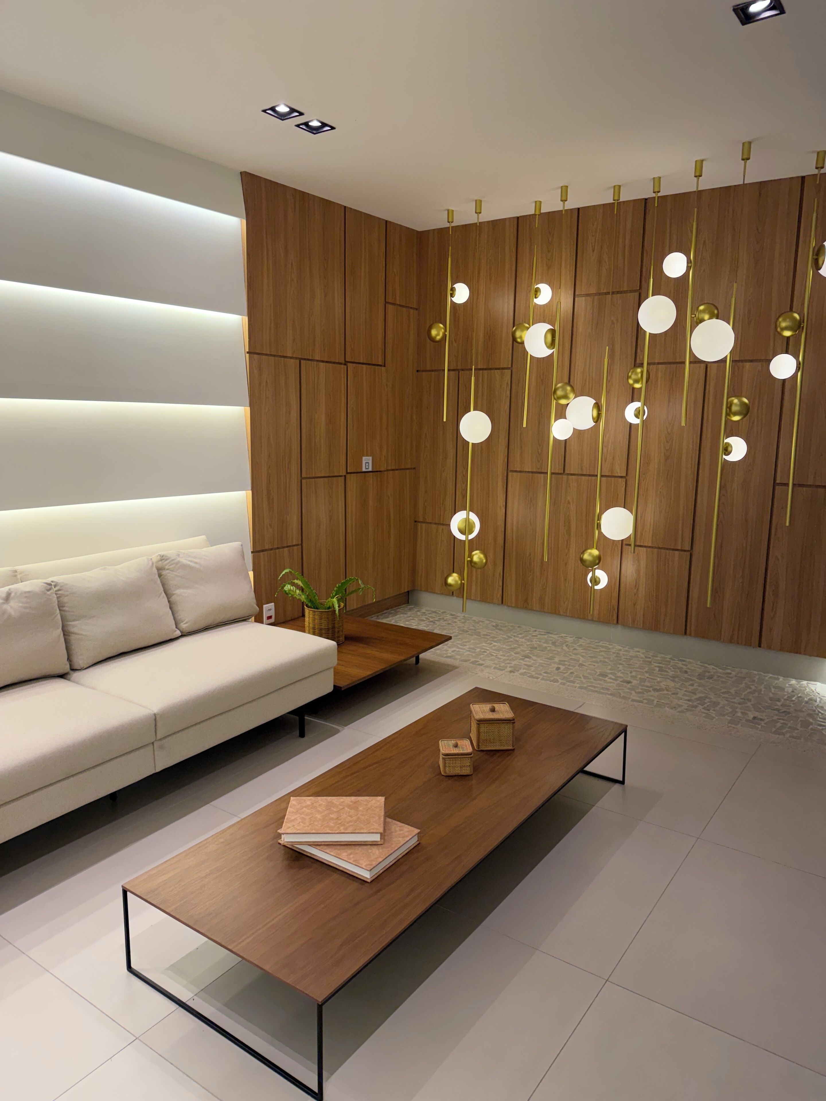 Una sala de estar moderna con un sofá, una mesa de centro de madera con libros, y una pared decorativa con luces colgantes.