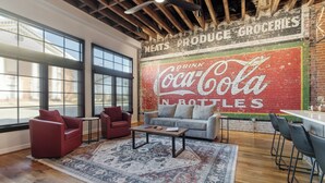A spacious room with large windows, a red Coca-Cola mural, and a wooden ceiling.
