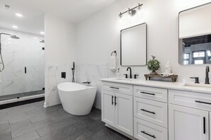A modern bathroom with a freestanding bathtub, a large mirror, and a vanity with drawers. - Downtown Spartanburg Apt. | Stay Fizzy (Spartanburg)