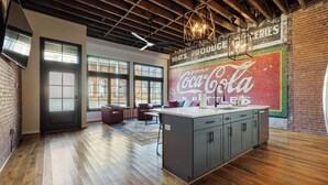 A spacious kitchen with a large island, wooden floors, and a Coca-Cola mural on the wall.