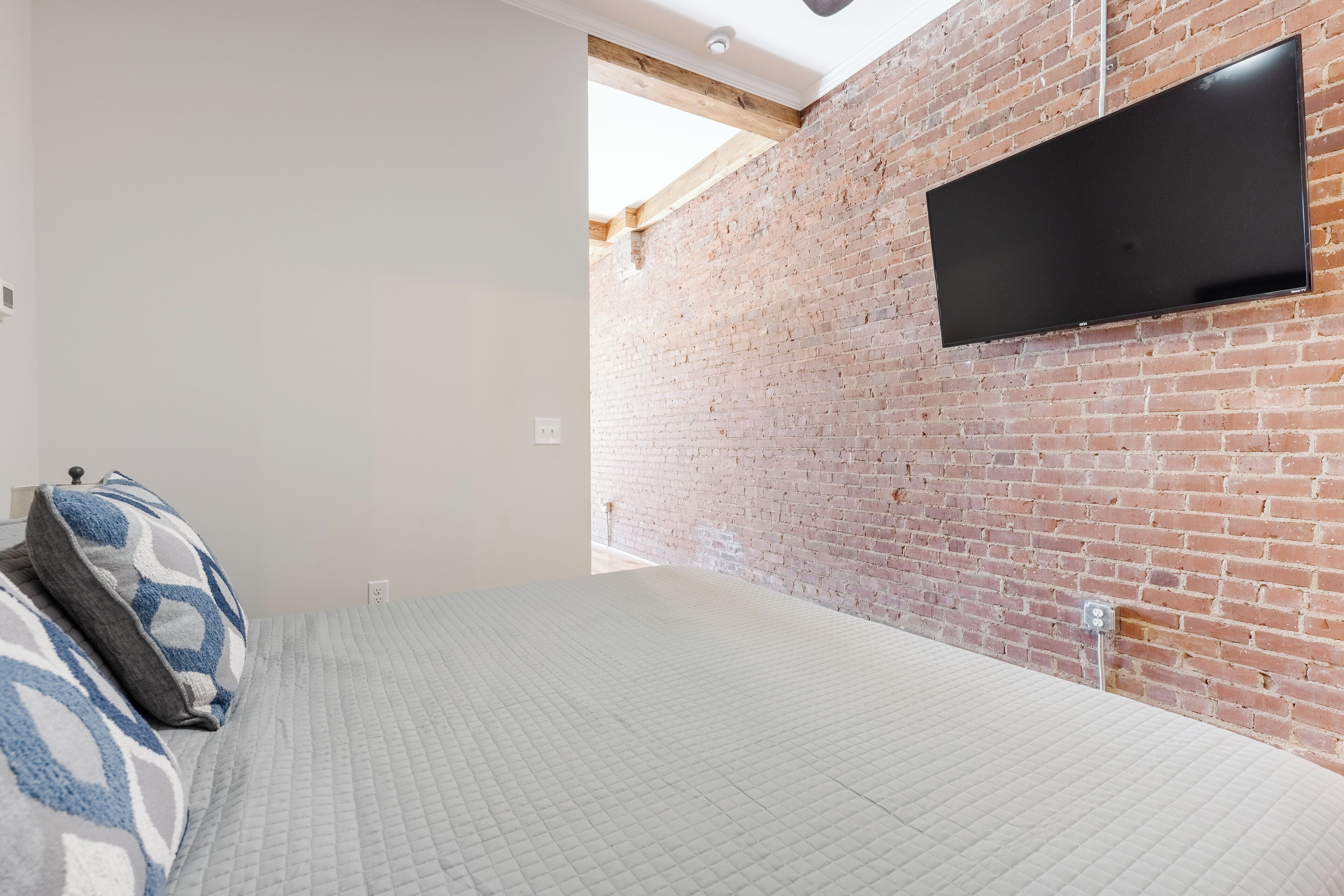 Een slaapkamer met een bakstenen muur, een flatscreen televisie die erop bevestigd is, een bed met beddengoed met een patroon en een plafondventilator.
