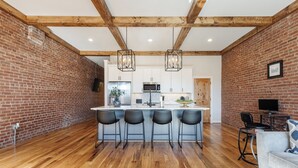 Una cocina moderna con una isla central, taburetes de bar y un comedor con sofá y televisor.