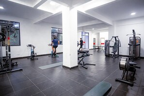 Ein Fitnessstudio mit unterschiedlichen Trainingsgeräten, einem großen Fenster und einem gefliesten Boden.