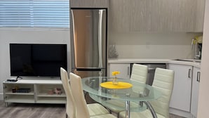 Een moderne keuken met een eethoek, met een glazen tafel, witte stoelen en een roestvrijstalen koelkast.