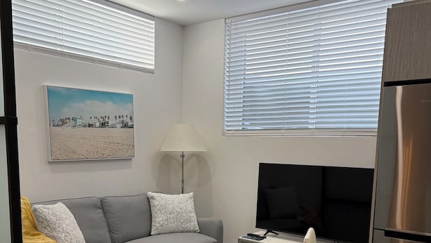 Een moderne woonkamer met een grijze bank, een televisie, een glazen tafel en een schilderij aan de muur.