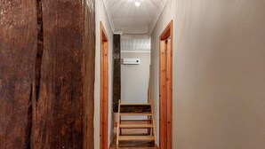 A narrow hallway with wooden doors on either side, a wooden bench in the center, and a white ceiling with a light fixture.