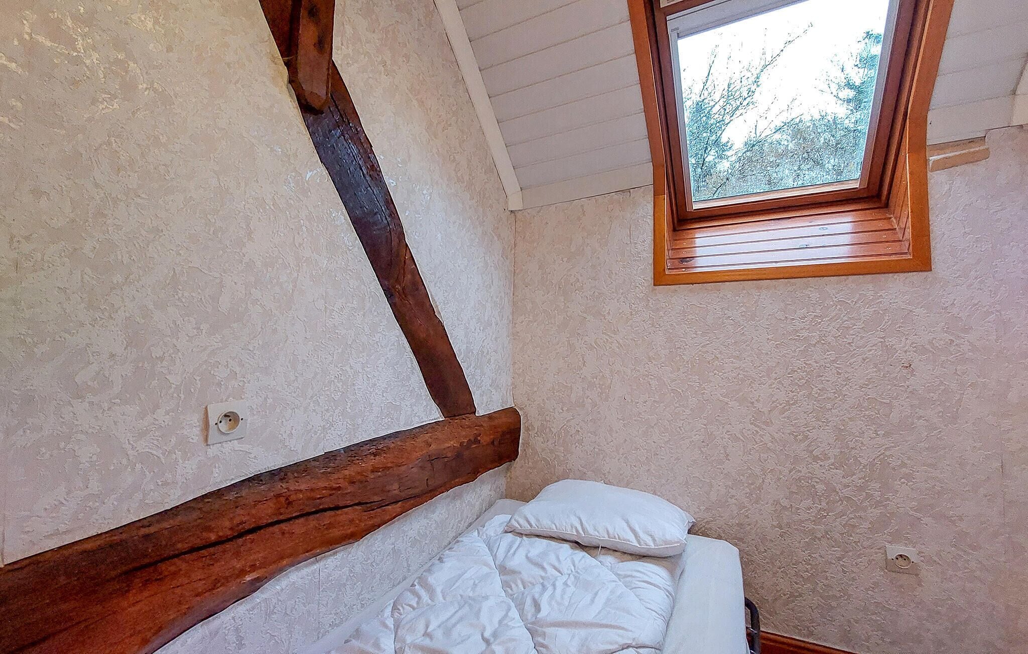 Ein Schlafzimmer mit einem Holzkopfteil, einem Einzelbett mit weißer Bettwäsche und einem Dachfenster.