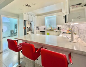 Una cocina moderna con armarios blancos, una isla central y taburetes rojos.