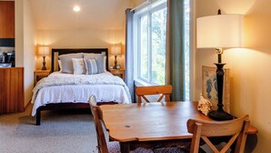 A bedroom with a bed, bedside lamps, a table, and chairs. - Haystack Luxury - Private Studio for Monthly Stays, Near Chapman Point, Deck + BBQ (Cannon Beach)