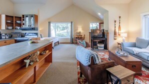 A spacious loft with a high ceiling, a kitchen area, a living room with a sofa and a fireplace, and a dining area. - Haystack Luxury - Private Studio for Monthly Stays, Near Chapman Point, Deck + BBQ (Cannon Beach)