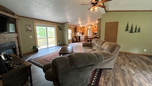 A spacious living room with a fireplace, a large sofa, and a dining area in the background. - Buck Run Cottage in the heart of Hocking Hills with Wi-Fi & Spectrum TV. (Logan)