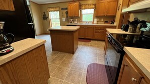 A kitchen with wooden cabinets, a central island, a dishwasher, and a stove. - Buck Run Cottage in the heart of Hocking Hills with Wi-Fi & Spectrum TV. (Logan)