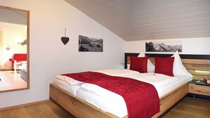 Une chambre à coucher avec un lit en bois, une literie blanche, des oreillers rouges et deux photographies en noir et blanc accrochées au mur.