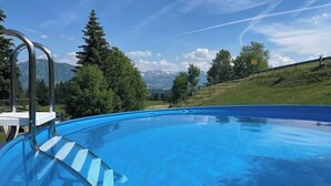 Une piscine avec un escalier en métal, entourée d’arbres et offrant une vue sur les montagnes.