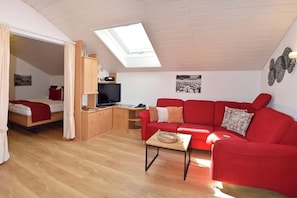 Ein gemütliches Zimmer mit einem roten Sofa, einem kleinen Tisch, einem Fernseher und einem Dachfenster.