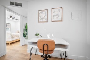 Een moderne kamer met een wit bureau, een bruine stoel en twee abstracte kunstwerken in lijsten aan de muur.