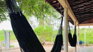 A hammock under a covered area with a tiled floor and a view of greenery outside.
