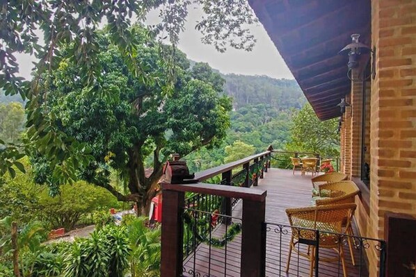A wooden deck with wicker chairs, overlooking a lush green forest and hills.