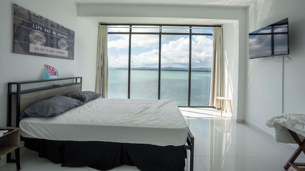 A bedroom with a large window, a bed, a TV, and a motivational poster. - Ocean Front Property (Naguabo)