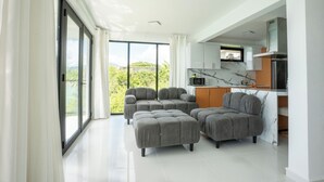 A modern living room with large windows, a kitchen area, and grey upholstered seating. - Ocean Front Property (Naguabo)