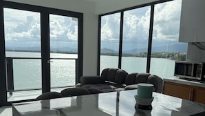 A modern kitchen with a marble countertop, a built-in microwave, and a view of a lake through large windows. - Ocean Front Property (Naguabo)