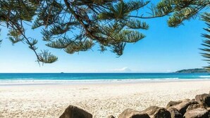 A beach with clear blue water, sandy shore, and large rocks in the foreground. - Billabelongil - 40A Childe St, Byron Bay (Byron)