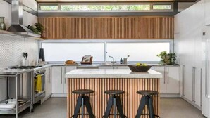 A modern kitchen with a central island, bar stools, a stainless steel range, and a large window. - Billabelongil - 40A Childe St, Byron Bay (Byron)