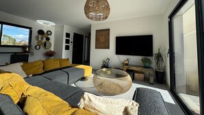 Een moderne woonkamer met een grote hoekbank, een ronde salontafel en een grote tv aan de muur.