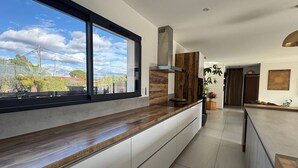 Een moderne keuken met een groot raam, witte kasten en een houten aanrecht.