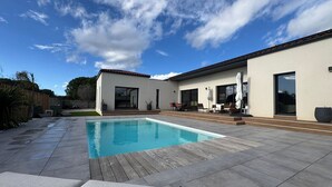Een modern huis met een zwembad, terrasmeubilair en een helderblauwe lucht.
