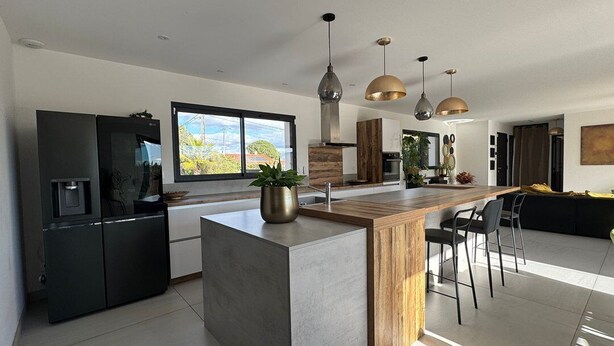 Een moderne keuken met een centraal eiland, hanglampen en een groot raam.