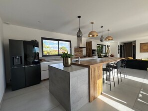 Eine moderne Küche mit Kochinsel, Pendelleuchten und einem großen Fenster.