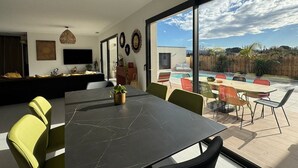 Een moderne woonkamer met een grote eettafel, comfortabele zitplaatsen en uitzicht op een achtertuin met een zwembad.